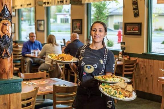Waitress smiles as she holds three plates of Black Bear Diner Wow Factor Meals